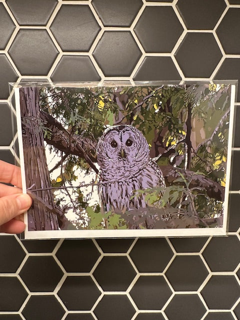 Person holding a card with a barred owl illustration against a tiled wall.