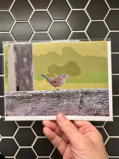 Hand holding a card with a wren illustration against a tiled wall background