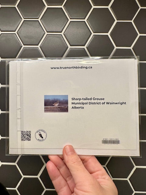 Hand holding a card with 'Sharp-tailed Grouse' information against a tiled wall background