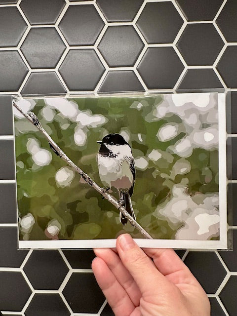 Hand holding a card with a chickadee illustration against a tiled wall background