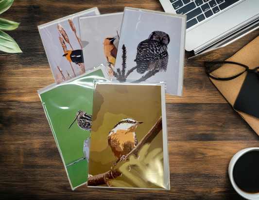 Set of greeting cards with bird designs on a wooden desk with a laptop and coffee cup.